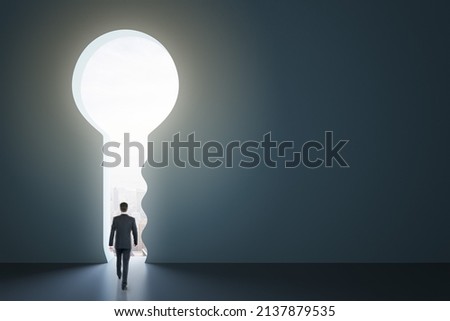 Back view of businessman standing in abstract key opening in wall with bright light and mock up place. Solution and decision concept Royalty-Free Stock Photo #2137879535