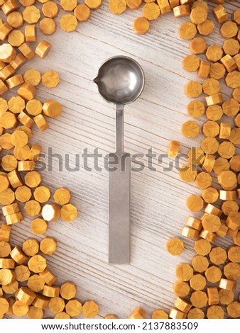 Sealing wax metal spoon and yellow gold sealing wax granules or beads a lot on wooden background. Vertical photo copy space, top view