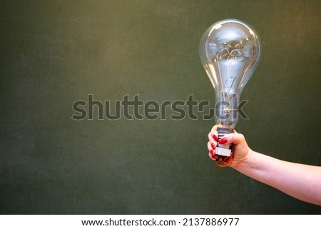 A large light bulb in the girl's hand against the background of the school blackboard.