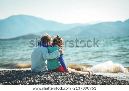Couple kids hug each other on sea beach. Children playing with sand on summer beach. Happy children run at sea beach. Kids are playing merrily. Boy and girl look on beautiful nature. Back view Royalty-Free Stock Photo #2137890961