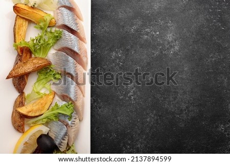 Pickled Herring with baked potatoes, onions and lettuce, on a dark background