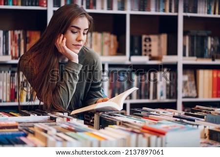 Young female customer reading a book in bookstore while buying some good literature. Woman picking a book to read. Royalty-Free Stock Photo #2137897061