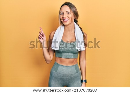 Beautiful hispanic woman wearing sportswear and towel with a big smile on face, pointing with hand finger to the side looking at the camera. 