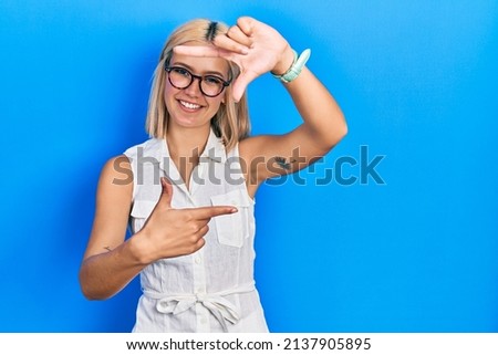 Beautiful blonde woman wearing glasses smiling making frame with hands and fingers with happy face. creativity and photography concept. 