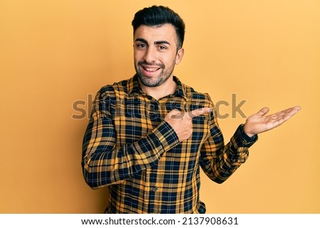 Young hispanic man wearing casual clothes amazed and smiling to the camera while presenting with hand and pointing with finger. 
