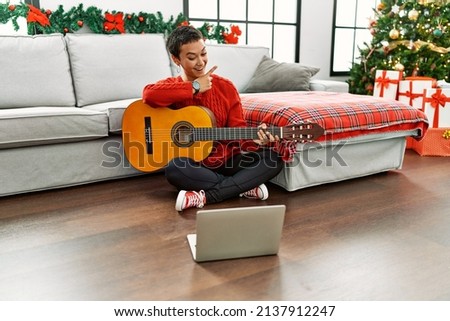 Hispanic woman with short hair learning classical guitar from online tutorial smiling happy pointing with hand and finger to the side 