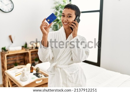 Young hispanic woman talking on the smartphone holding credit card at beauty center