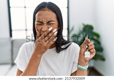 Young hispanic woman holding keys of new home bored yawning tired covering mouth with hand. restless and sleepiness. 