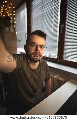 Wide angle selfie of a man working remotely with blurred boke background. Bearded guy wears a round glasses