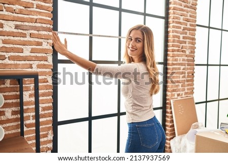 Young blonde woman smiling confident measuring window at new home