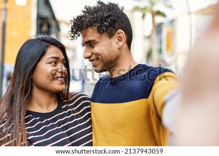 Young latin couple smiling happy and hugging make selfie by the camera at the city.