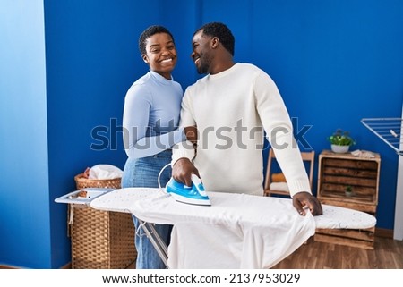Man and woman couple smiling confident ironing clothes at laundry room