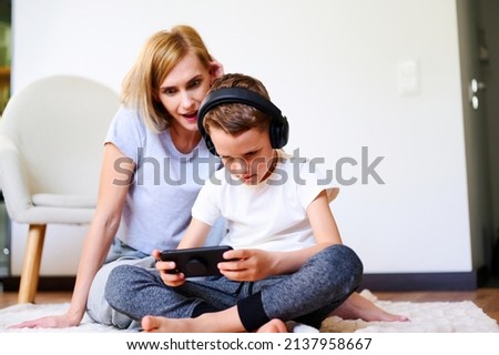Caucasian boy with mother plays phone on the floor with headphones watching cartoons, listening to music, playing games