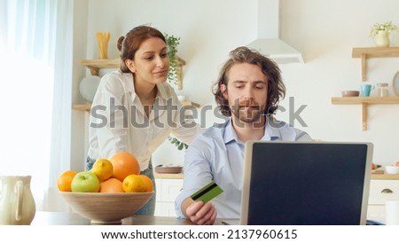 Young Couple Shopping Online Using a Credit Card Payment Purchasing on a Laptop Together Sitting at the Bright Kitchen. Couple Celebrating With Fun Expressive Doing Winner Gesticulating Hands.
