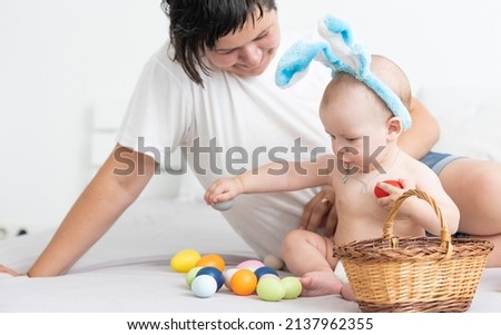 happy family celebrating easter mother and baby bunny ears at home with colorful eggs