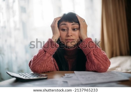 Sad woman holding her head over utility bills. The concept of rising prices for heating, gas, electricity. A young worried dissatisfied girl looks at papers does not expect a high cost of services. Royalty-Free Stock Photo #2137965233