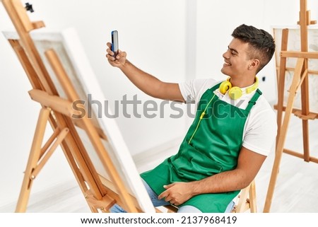 Young hispanic man smiling confident make selfie by the smartphone at art studio