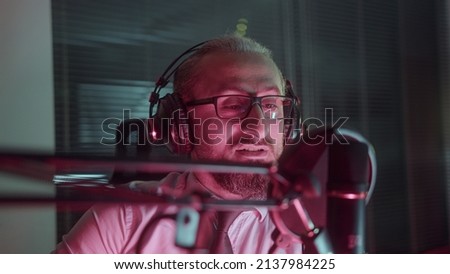 Podcast Recording in the Red Lightroom. Middle-aged man with glasses is recording audio.