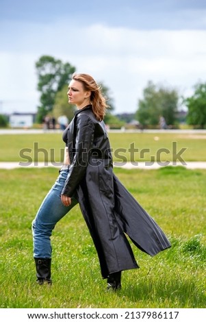 young brunette woman in jeans and black leather coat standing on in a park