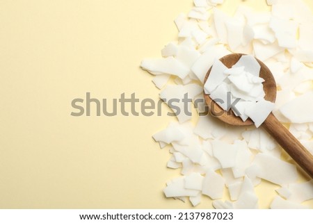 Wooden spoon and soy wax flakes on beige background, flat lay with space for text. Homemade candle material