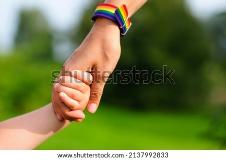 parent holds the hand of a small child. mother holding baby's hand. rainbow lgbt bracelet on parents hand.  Royalty-Free Stock Photo #2137992833