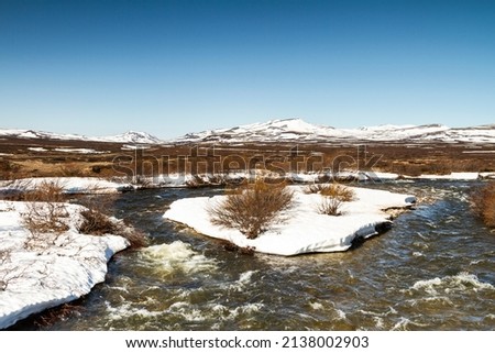Spring scenery in the Dovrefjell, Norway, with creek, rocks, hills, mountains, and patches of snow Royalty-Free Stock Photo #2138002903