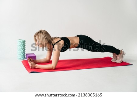 Portrait of a beautiful young European woman doing sports in the studio on a white background. Girl in leggings and a black top, Plank exercise pose on the elbows on mat with a block. Yoga, fitness