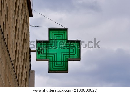 green cross-shaped pharmacy sign with sky in the background