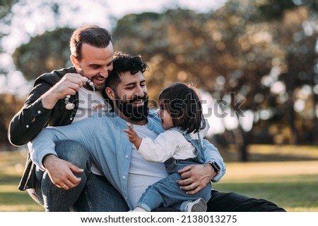 Male gay family hugging and playing with their little daughter in the park. Royalty-Free Stock Photo #2138013275