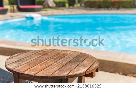 Round Wooden Table and blurred empty swimming Pool Outdoor on day light Royalty-Free Stock Photo #2138016325