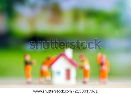 blurred photo of miniature worker working with tiny home model  on wooden floor over blurred garden background.