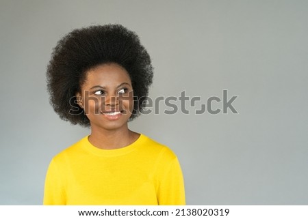 Smiling young african woman in yellow sweater looking away to copy space. Friendly young black girl look at empty space for advertising, offering, product, promotion, sale stand over studio grey wall.