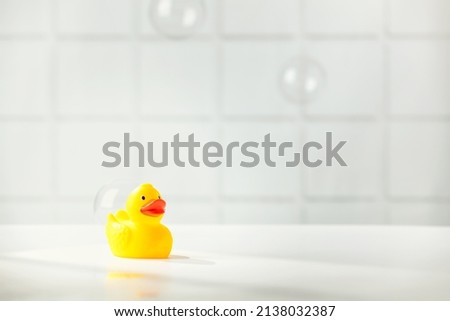 Cute rubber duck on white bathroom countertop with soap bubbles, space for text, horizontal composition