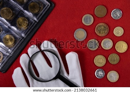 Collection of coins and collector white gloves and magnifying glass on red Royalty-Free Stock Photo #2138032661