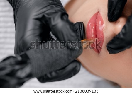Permanent Macro photo of process of applying makeup tattoo of red on lips woman, top view.