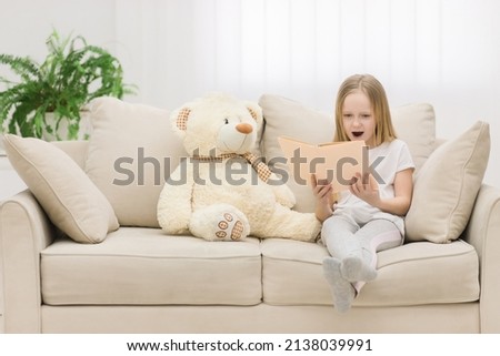 Photo of blond girl reading a book to her toy plush friend.