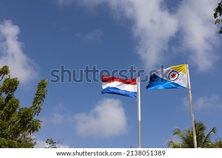 Flag of Bonaire and Netherlands flying in the wind on the blue sky background.
