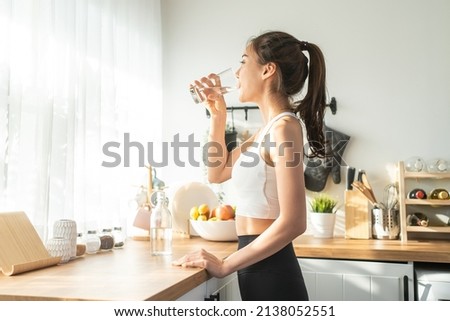 Asian beautiful woman in sportswear drink water after exercise at home. Young thirsty active sport girl takes a sips of clean mineral natural in cup after workout for health care in kitchen in house. Royalty-Free Stock Photo #2138052551