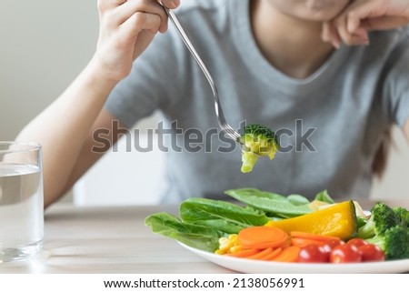 unhappy asian women is on dieting time looking at broccoli on the fork. girl do not want to eat vegetables and dislike taste Royalty-Free Stock Photo #2138056991