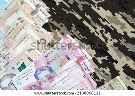 Ukrainian hryvnya bills on fabric with texture of Ukrainian military pixeled camouflage. Cloth with camo pattern in grey, brown and green pixel shapes. Official uniform of Ukrainian soldiers close up
