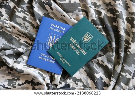 Ukrainian military ID and foreign passport on fabric with texture of pixeled camouflage. Cloth with camo pattern in grey, brown and green pixel shapes with Ukrainian army personal token and passport.
