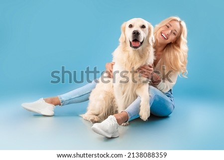 Love And Care Concept. Cheerful young lady patting her happy labrador spending time together, embracing pet, posing looking at camera sitting on the floor isolated on blue background, full body length Royalty-Free Stock Photo #2138088359