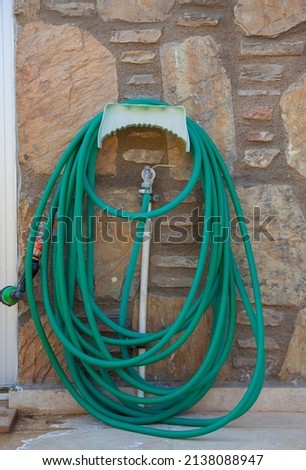 Green long garden hose.  Coiled garden hose hanging on faucet against the stone wall. Front view, vertical and close up.