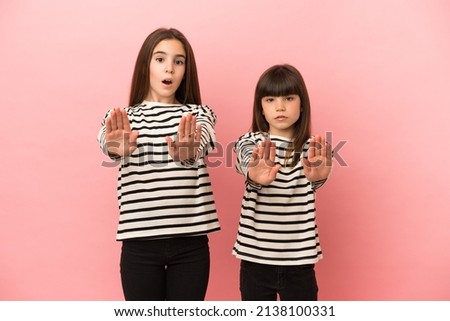 Little sisters girls isolated on pink background making stop gesture for disappointed with an opinion