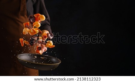 A professional chef prepares assorted seafood - octopus, shrimp and pieces of red fish. Seafood in frozen flight on a black background. Sea food. Healthy food, vegetarian food. Royalty-Free Stock Photo #2138112323