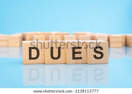 word Dues on wooden cubes on blue background. the inscription on the cubes is reflected from the surface. business concept.