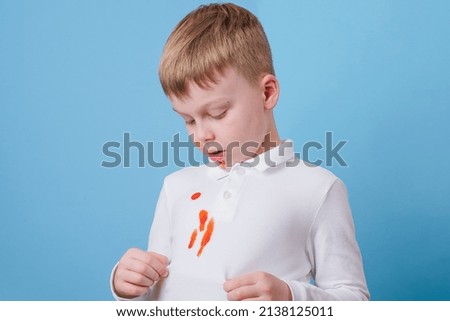Boy showing a red stain spilled from tomato sauce on white clothes. The concept of cleaning stains on clothes. High quality photo Royalty-Free Stock Photo #2138125011