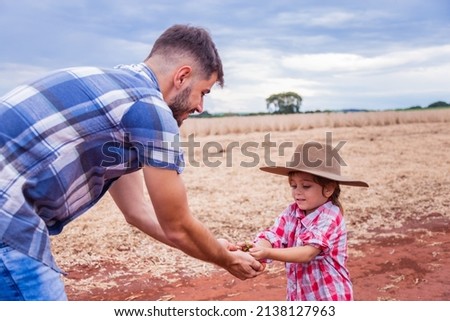little girl passing a plant from her hands to her farmer father's hand.