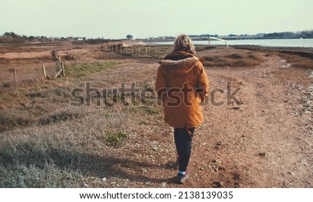 Woman walking along shoreline next to a river Royalty-Free Stock Photo #2138139035