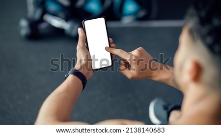Unrecognizable Male Using Cellphone With White Screen At Gym, Mockup Image Of Sporty Man Browsing Mobile App On Blank Phone While Relaxing After Training In Sport Club, Over Shoulder View Royalty-Free Stock Photo #2138140683